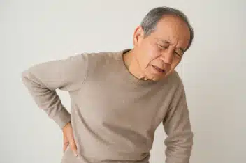 腰痛の高齢者。腰に手を当てている。